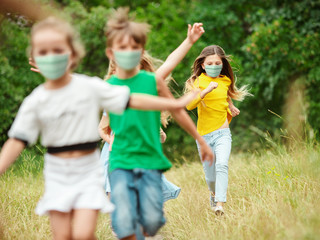 Fototapeta premium Happy little kids wearing protective face mask jumping and running on meadow, forest. Looks happy, cheerful, sincere. Copyspace. Childhood, pandemic concept. Healthcare, coronavirus pandemic.