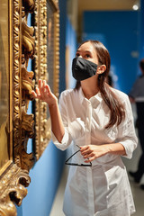 Woman visitor wearing an antivirus mask in the historical museum looking at pictures.