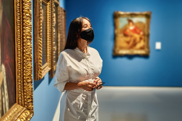Woman visitor wearing an antivirus mask in the historical museum looking at pictures.