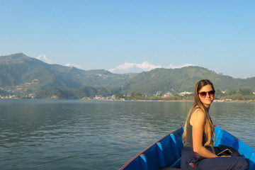 Fototapeta premium A woman sitting in a blue boat and enjoying a tour across Phewa Lake in Pokhara, Nepal. Behind her there are high, snow capped Himalayas with Mt Fishtail (Machhapuchhare) between them. Relaxation