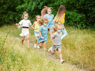 Happy little kids wearing protective face mask jumping and running on meadow, forest. Looks happy,...