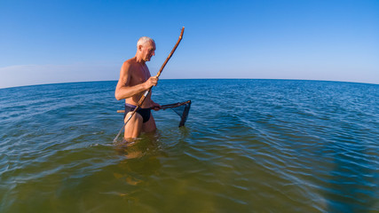 Man hunts with a homemade spear and a homemade helper in shallow water