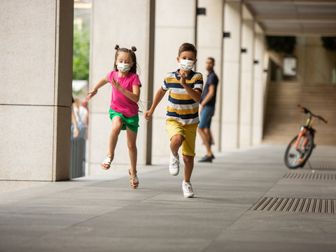 Happy little kids wearing protective face mask jumping and running on city street. Looks happy, cheerful, sincere. Copyspace. Childhood, pandemic concept. Healthcare, coronavirus pandemic.