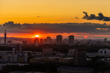Black silhouettes of buildings are on a red sky background with orange and yellow sunset