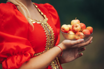 A young girl dressed in national Russian clothes of red color outdoors holding a plate with apples in her hand Art grain and noise on photo