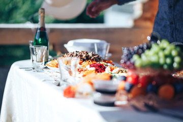 Long table covered with a tablecloth on which there is a lot of food, food in plates