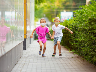 Happy little kids wearing protective face mask jumping and running on city street. Looks happy, cheerful, sincere. Copyspace. Childhood, pandemic concept. Healthcare, coronavirus pandemic.