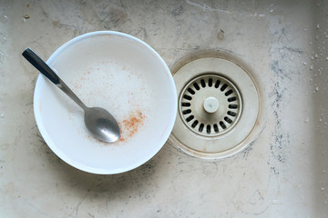 Dirty wash basin sink plug hole and a leftover empty bowl 