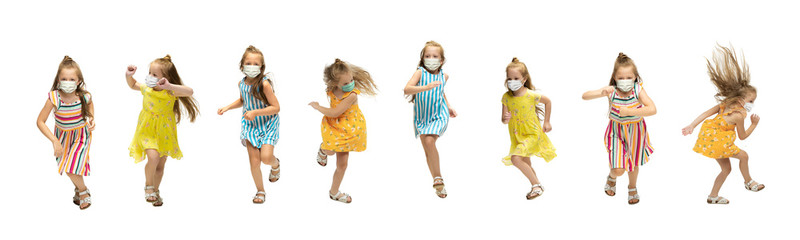 Happy 2 little girls wearing protective face mask jumping and running isolated on white background. Looks happy, cheerful, sincere. Copyspace. Childhood, pandemic concept. Healthcare, coronavirus