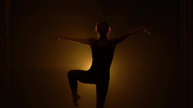 Silhouette of sporty young women practicing acrobatic. A girl gymnast doing gymnastic exercises. Shot in studio with smoke and yellow soft light. Close up.
