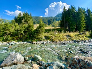 Beautiful view on the skiing region of Saalbach-Hinterglemm in summer with trees and a creek with clear water used by people for refreshment on a sunny summer day.