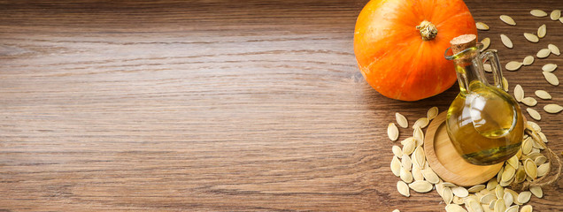 Pumpkin oil in a bottle, pumpkin, pumpkin seeds on a background of wood texture.With space for text...