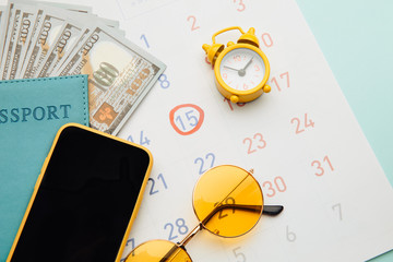Calendar with passport, sunglasses and smartphone on blue background. Vacation planning concept.