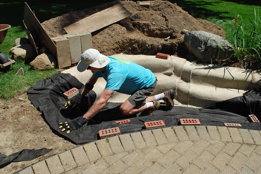 Man Installing Pond Underlayment For His Backyard Water Feature Project To Prevent Punctures