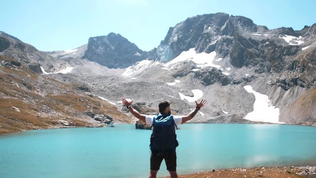 Traveler in a white T-shirt solemnly makes a helpless gesture near a mountain lake on the top of a mountain