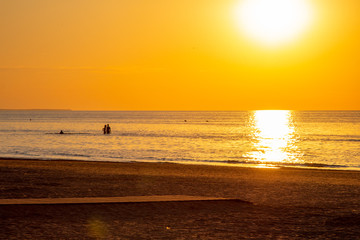 Beautiful sunset at the sea. Young people walk along the beach. People are watching the sunset. Sea and red-yellow sky. Silhouettes of people on the background of the sunset. In the evening by the sea