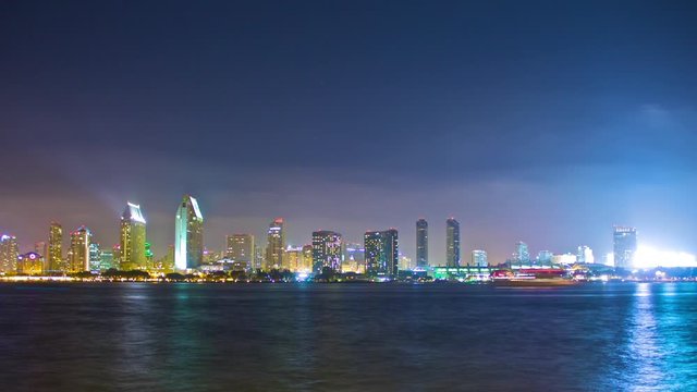 Night timelapse of downtown San Diego, CA skyline viewed from across the water on Coronado Island. Boats pass by in the foreground and a fireworks show is displayed.