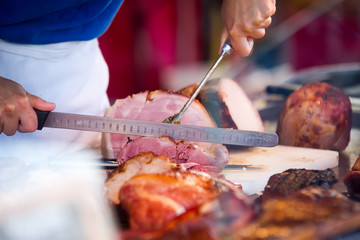Chef cutting slices of grilled pork with long ham knife. Red background