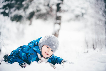 Fototapeta na wymiar Happy little kid is playing in snow, good winter weather. Little boy having fun in the snow.