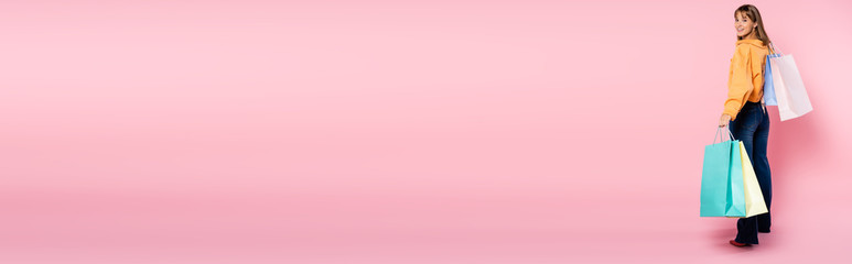 Horizontal image of woman with shopping bags looking at camera on pink background with copy space