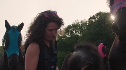 Young woman farmhand greets & pets a family of horses in meadow during evening