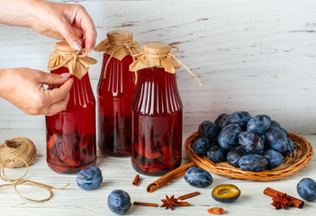 Homemade plum compote with cinnamon and star anise. Delicious healthy vitamin drink. Women's hands, Jars and fresh berries on a light wooden table. Selective focus, copy space