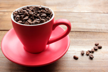 Cup of coffee beans on a wooden table. Close-up of coffee beans in a red cup on wood background with copy space.