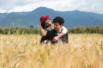 Fototapeta na wymiar Couple in love having fun in a wheat field - Happy young Hispanic couple enjoying time together in the field - Man carrying his girlfriend on his back while enjoying the summer
