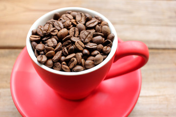 Cup of coffee beans on a wooden table. Close-up of coffee beans in a red cup on wood background with copy space.