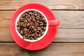 Cup of coffee beans on a wooden table from above. Flat lay of coffee beans in a red cup on wood background with copy space.