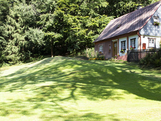 Old romantic cottage at dawn with the shadow of a tree on a mown meadow