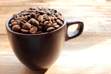 Cup of coffee beans on a wooden table. Close-up of coffee beans in a brown ceramic cup on wood...