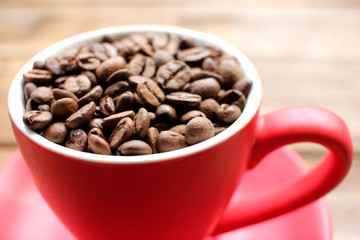 Cup of coffee beans on a wooden table. Close-up of coffee beans in a red cup on wood background with copy space.