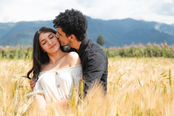 Loving couple kissing in the middle of a wheat field - Hispanic young people enjoying nature at sunset