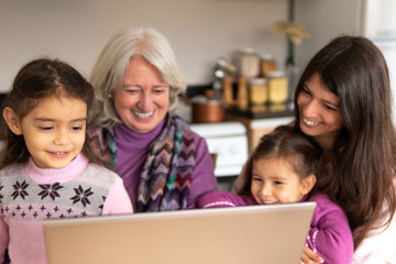 Happy cheerful female multigenerational family with laptop engaged in fun activity in kitchen home,...