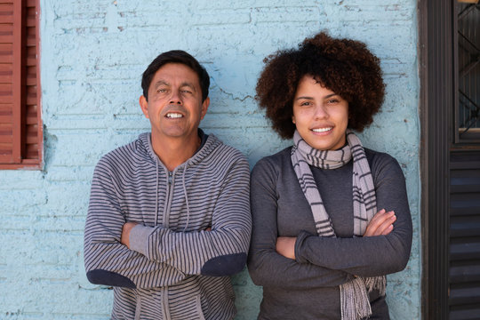 Portrait Of Brazilian Adult Daughter And Older Father With Arms Crossed Looking At Camera Outside Humble Home Family, Together Concept.