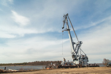 Big industrial ship with crane at river port near pile of logs