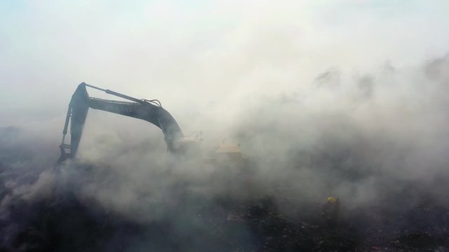 Aerial view of a excavator, in middle of smoke, trying to extinguish a wildfire, in Los Angeles, California, USA - static, drone shot