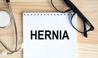 HERNIA - inscription in a notebook, next to a tablet and a stethoscope. A medical concept.