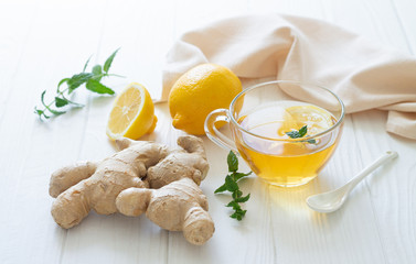 Cup of hot tea with ginger root, lemon and mint on white wooden table