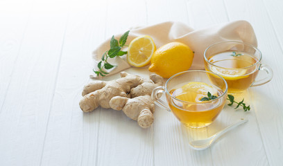 Two cups of healthy ginger tea with mint leaves and lemon on white table