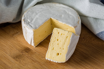 Fresh Brie cheese and a slice close up on wooden board