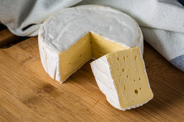 Fresh Brie cheese and a slice close up on wooden board