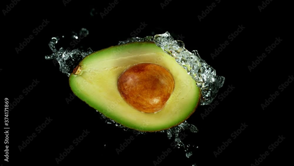 Wall mural Super Slow Motion Shot of Half Avocado with Splashing Water Isolated on Black Background at 1000fps.