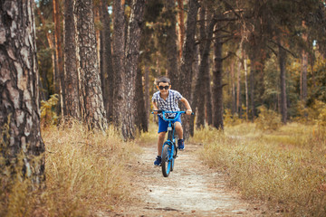 Happy kid cyclist rides in the forest on a bike.