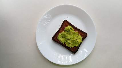Baked toast with avocado on a white plate. Vegan food. Vertical photo