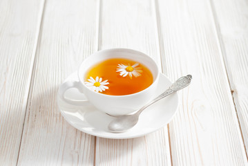 White cup of herbal tea with chamomile flowers on the white wooden background. Natural organic alternative medicine