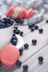Yummy pink macaroon placed near bowl with ripe blueberries on table at home