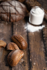 From above fresh rye buns placed on wooden table near loaf of bread and jar of flour in rustic kitchen