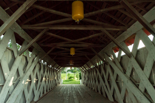 Inside view of covered bridge in Madison County, Winterset, Iowa, with trusses, running boards, yellow lights, and light at the end of the tunnel  Royalty free stock photo